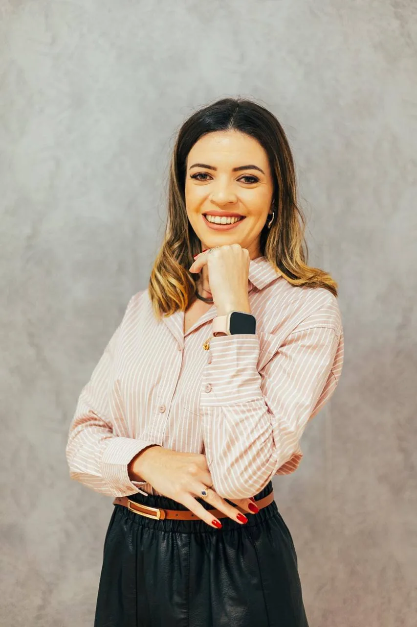 Anna Gabrielle em pé, usando camisa rosa listrada